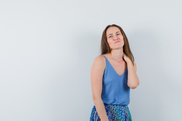 Señora joven que sufre de dolor de cuello en camiseta, falda y mirando molesto, vista frontal.