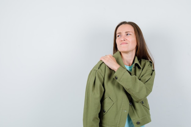 Señora joven que sufre de dolor en el hombro en camiseta, chaqueta y con mal aspecto, vista frontal.