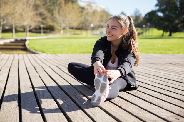 Señora joven sonriente que estira la pierna al aire libre