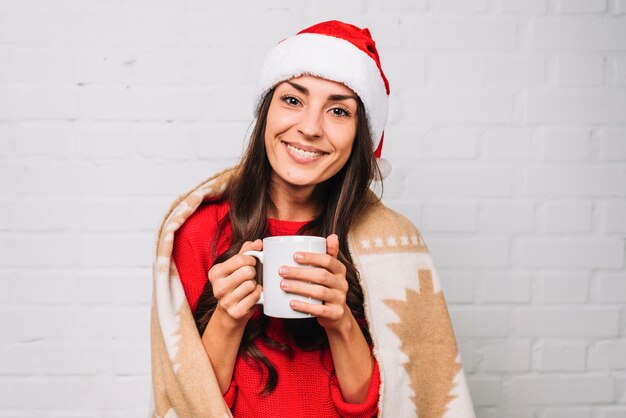 Señora joven sonriente en sombrero y tela escocesa del partido con la taza