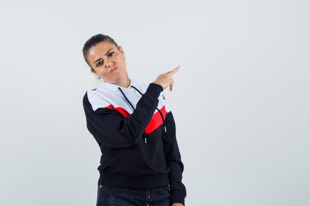 Señora joven en sudadera colorida apuntando hacia atrás, vista frontal.