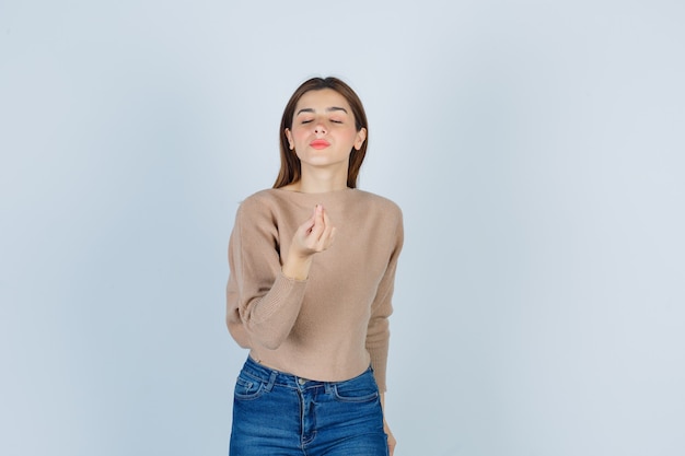 Señora joven en suéter beige, jeans mostrando un gesto delicioso y mirando complacido, vista frontal.