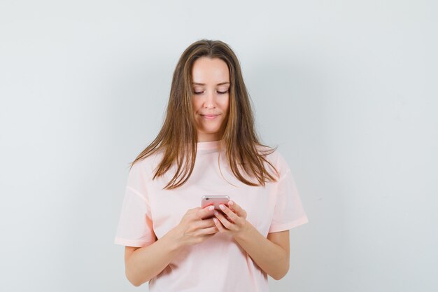 Señora joven con teléfono móvil en camiseta rosa y mirando alegre, vista frontal.