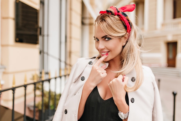 Foto gratuita señora linda con peinado de moda y manicura roja sonriendo juguetonamente. modelo de mujer rubia en elegante chaqueta y camisa negra divirtiéndose al aire libre.