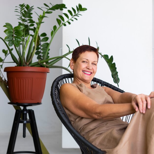 Señora madura sonriente con planta detrás