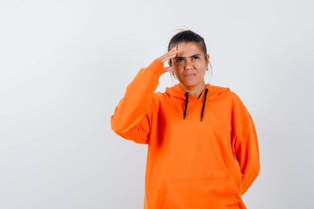 Señora manteniendo la mano sobre la cabeza en una sudadera con capucha naranja y luciendo soñadora