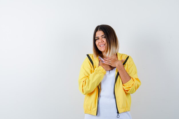 Señora manteniendo las manos en el pecho en camiseta, chaqueta y mirando alegre, vista frontal.