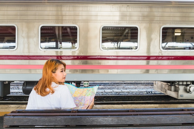 Señora con mapa en asiento cerca de tren en plataforma