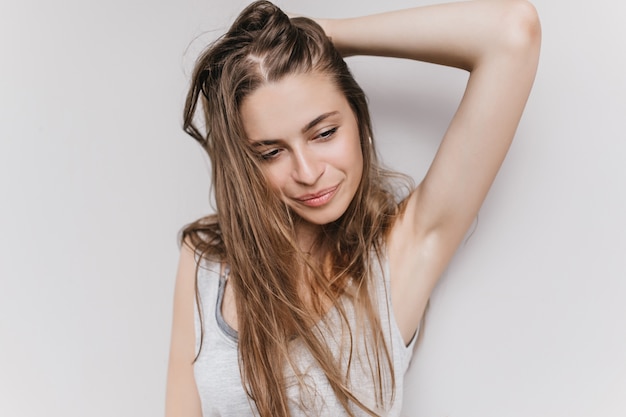 Señora maravillosa delgada jugando con su pelo largo y mirando a otro lado. Foto interior de una niña caucásica extasiada aislada con expresión facial inspirada.