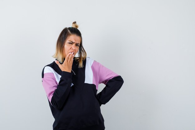 Señora maravillosa que lleva a cabo la mano en la boca en una sudadera y que parece sorprendida.