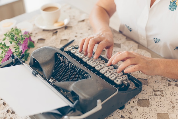Señora mayor escribiendo en máquina de escribir en casa con camisa blanca durante el día