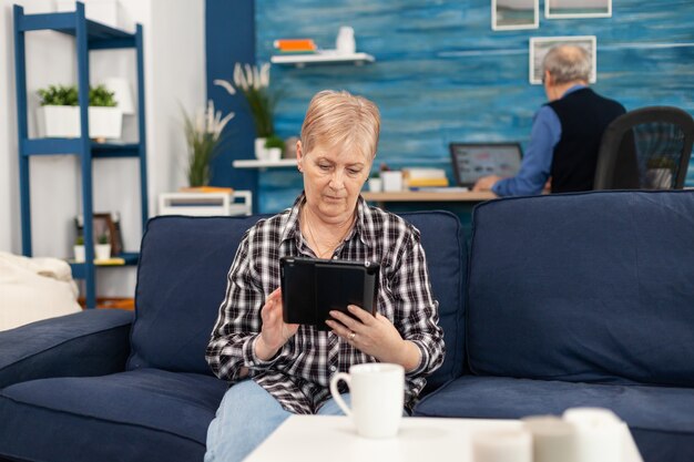 Señora de mediana edad relajándose en el sofá leyendo en tablet pc disfrutando de contenido