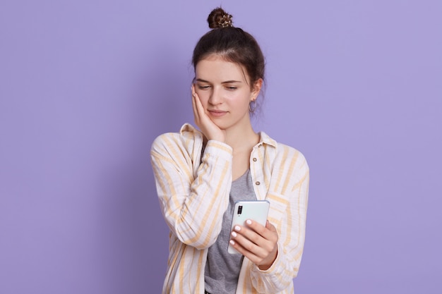 Señora molesta sosteniendo el teléfono móvil en las manos y mirando su pantalla con expresión facial triste