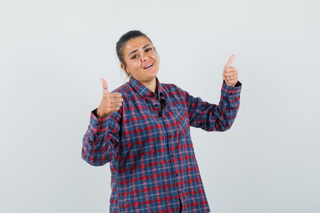 Señora mostrando doble pulgar hacia arriba en camisa casual y mirando confiada. vista frontal.