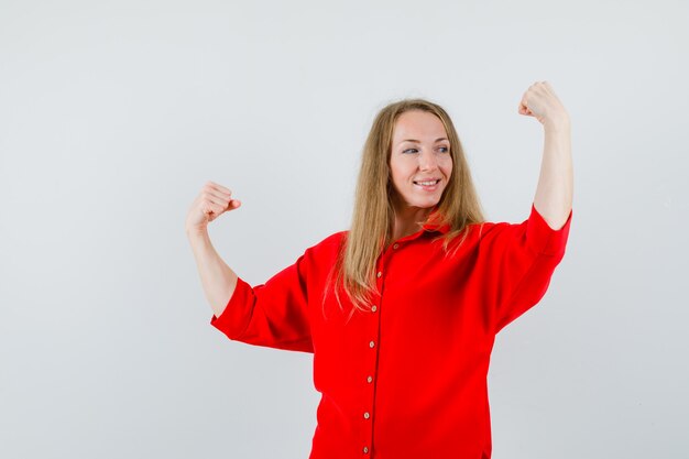 Señora mostrando gesto de ganador en camisa roja y mirando confiado.