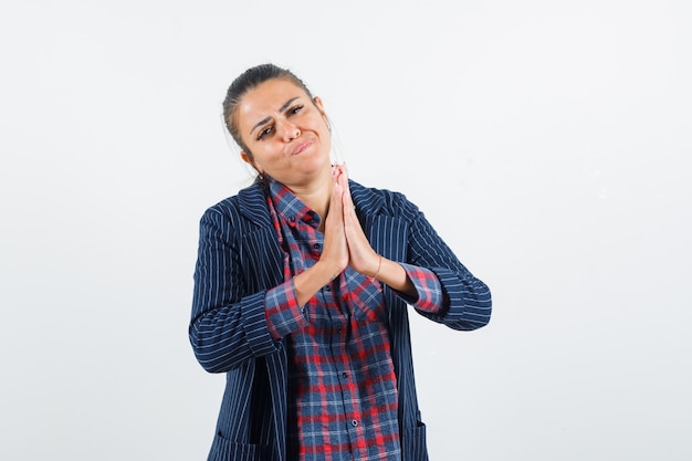 Señora mostrando gesto de namaste en camisa, chaqueta y mirando esperanzado, vista frontal.