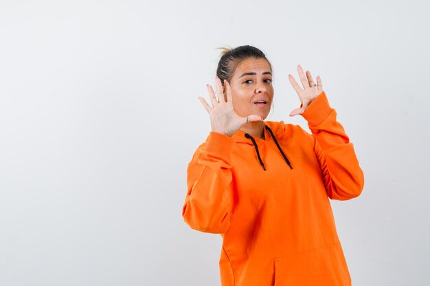 Señora mostrando las palmas en gesto de rendición en sudadera con capucha naranja y mirando confiada