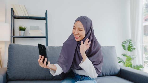 Señora musulmana usa hijab usando videollamada telefónica hablando con pareja en casa.