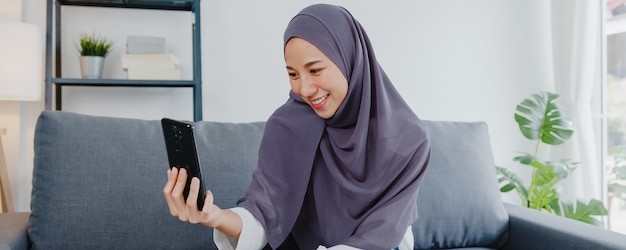 Señora musulmana usa hijab usando videollamada telefónica hablando con pareja en casa.