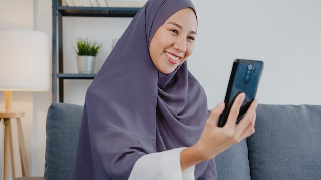 Señora musulmana usa hijab usando videollamada telefónica hablando con pareja en casa.