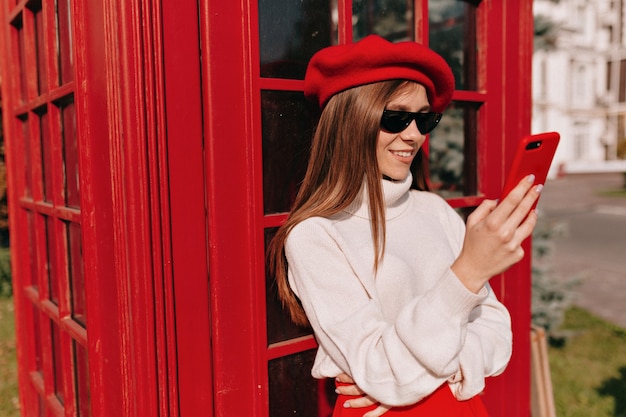 Señora muy encantadora vestida con traje francés de pie con smartphone