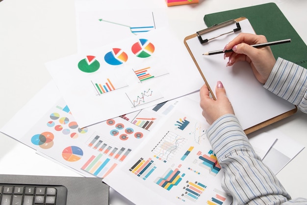 Señora de negocios de marketing en camisa a rayas en la oficina con computadora tomando notas mirando gráficos