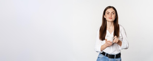 Foto gratuita señora de la oficina de la mujer de negocios joven moder sosteniendo la taza con té de café y sonriendo de pie contra pentecostés