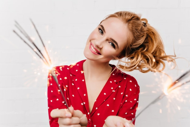 Señora de ojos azules riendo mientras agita las luces de bengala. Modelo de mujer caucásica rubia de primer plano con luces de bengala en la mañana de año nuevo.