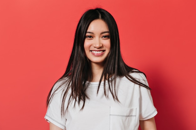 Señora con ojos marrones está sonriendo en la pared roja