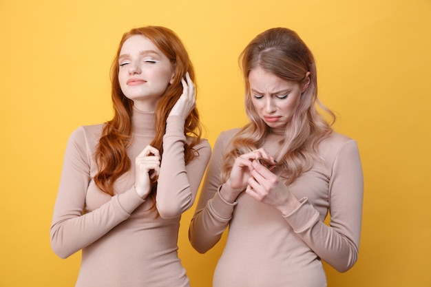 Señora pelirroja feliz tocando su cabello cerca de una mujer rubia triste