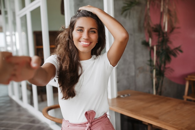 Señora de pelo largo en camiseta blanca está sonriendo contra windows