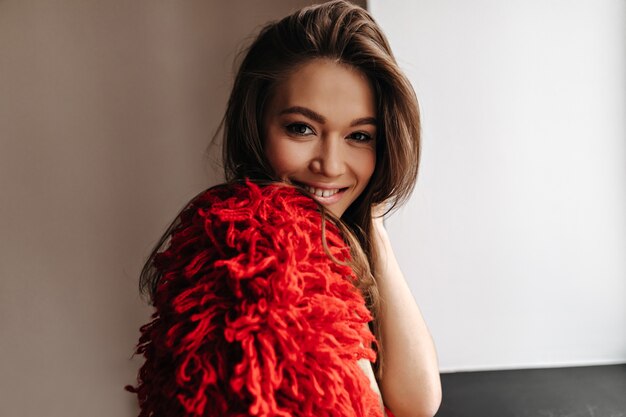 Señora de pelo oscuro con ojos marrones en chaqueta roja de lana mirando a la cámara con una sonrisa.