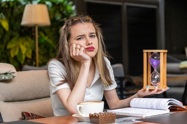 Señora pensativa que sostiene el reloj de arena y que mira la cámara