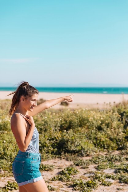 Señora de pie a la orilla del mar y mostrando la mano hacia adelante