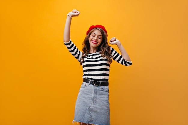 Foto gratuita señora positiva en boina y camisa sonriendo sobre fondo naranja. mujer elegante de buen humor con cabello ondulado bailando sobre fondo aislado.