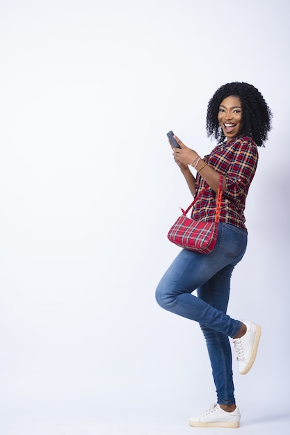 Señora que parece emocionada y feliz usando su teléfono, llevando un bolso.