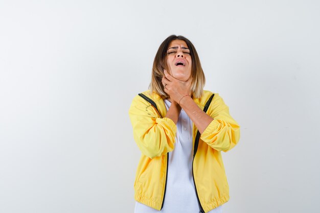 Señora que sufre de dolor de garganta en camiseta, chaqueta y aspecto enfermo, vista frontal.