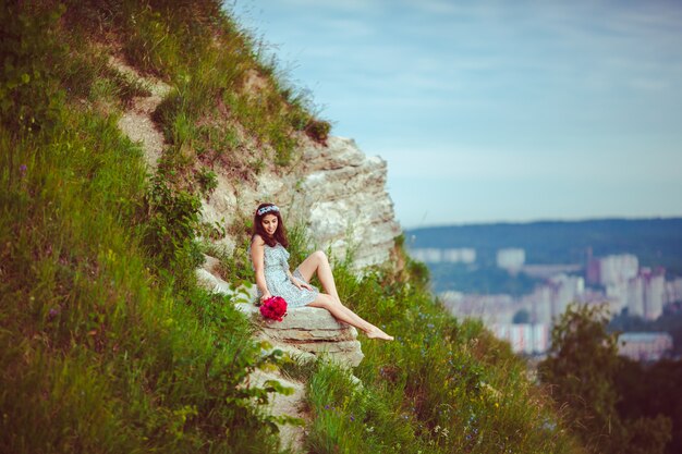 Señora con el ramo rojo se sienta en la colina verde