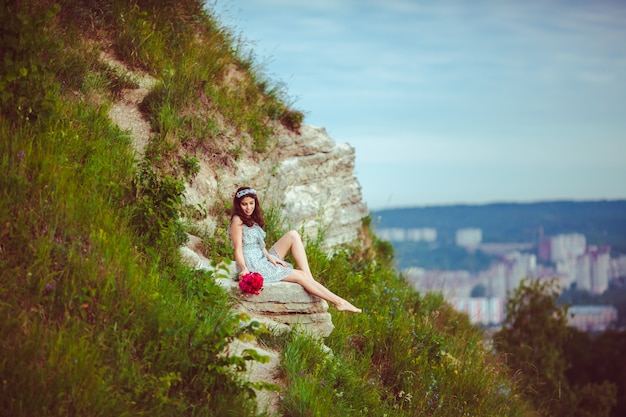 Señora con el ramo rojo se sienta en la colina verde