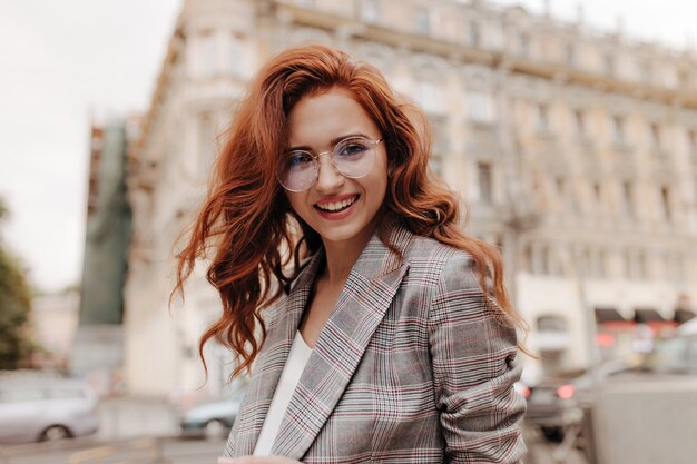 Señora rizada en anteojos sonriendo y posando afuera