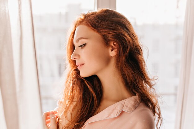 Señora romántica de pelo largo posando en casa. Retrato de muchacha atractiva pensativa del jengibre.