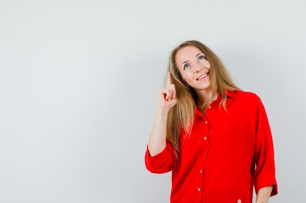 Señora rubia apuntando hacia arriba con camisa roja y mirando alegre.