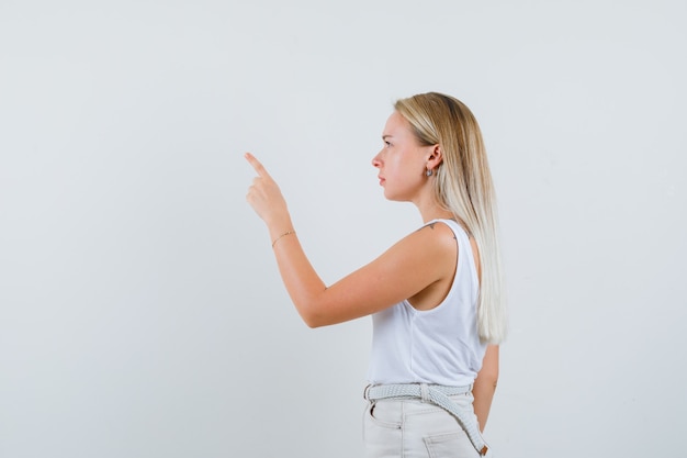 Foto gratuita señora rubia apuntando hacia arriba en camiseta, pantalones y mirando enfocado. .