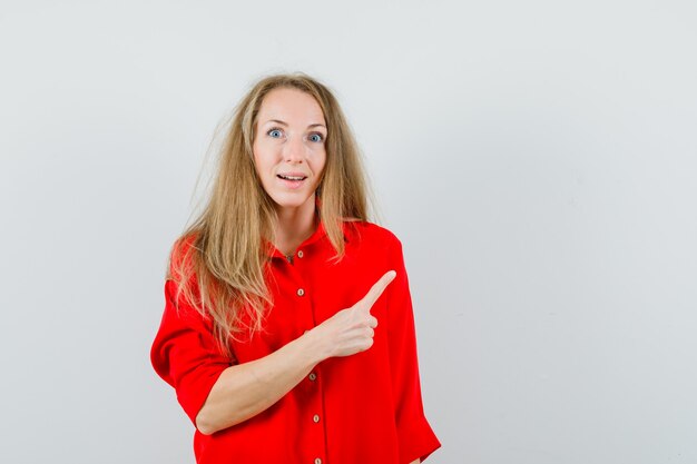 Señora rubia apuntando a la esquina superior derecha con camisa roja y mirando asombrado,