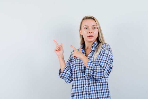 Señora rubia apuntando a la esquina superior izquierda en camisa casual y mirando confiada