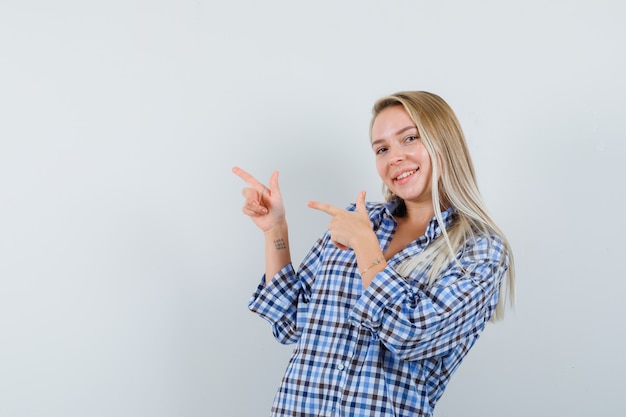 Señora rubia apuntando a la esquina superior izquierda en camisa casual y mirando feliz