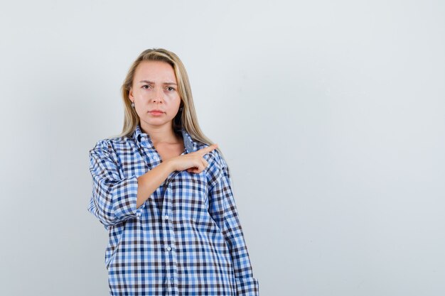 Señora rubia apuntando a un lado en camisa casual y mirando triste