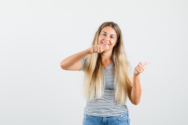 Señora rubia apuntando a un lado en camiseta y mirando alegre, vista frontal.