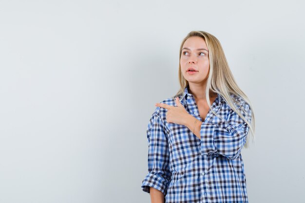 Señora rubia apuntando hacia el lado izquierdo en camisa casual y mirando pensativa