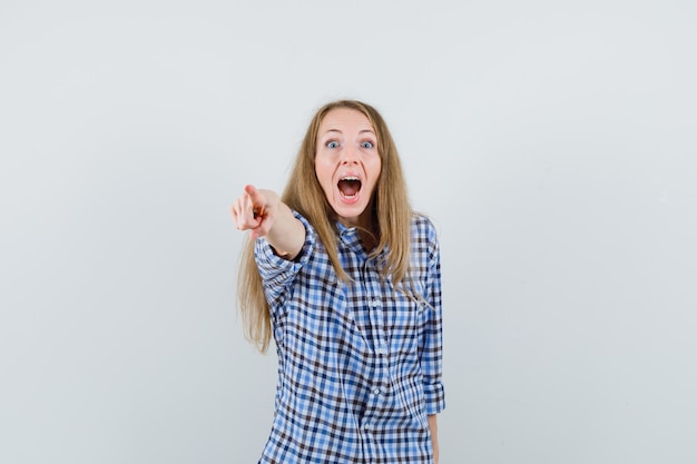 Señora rubia en camisa apuntando a la cámara mientras grita,